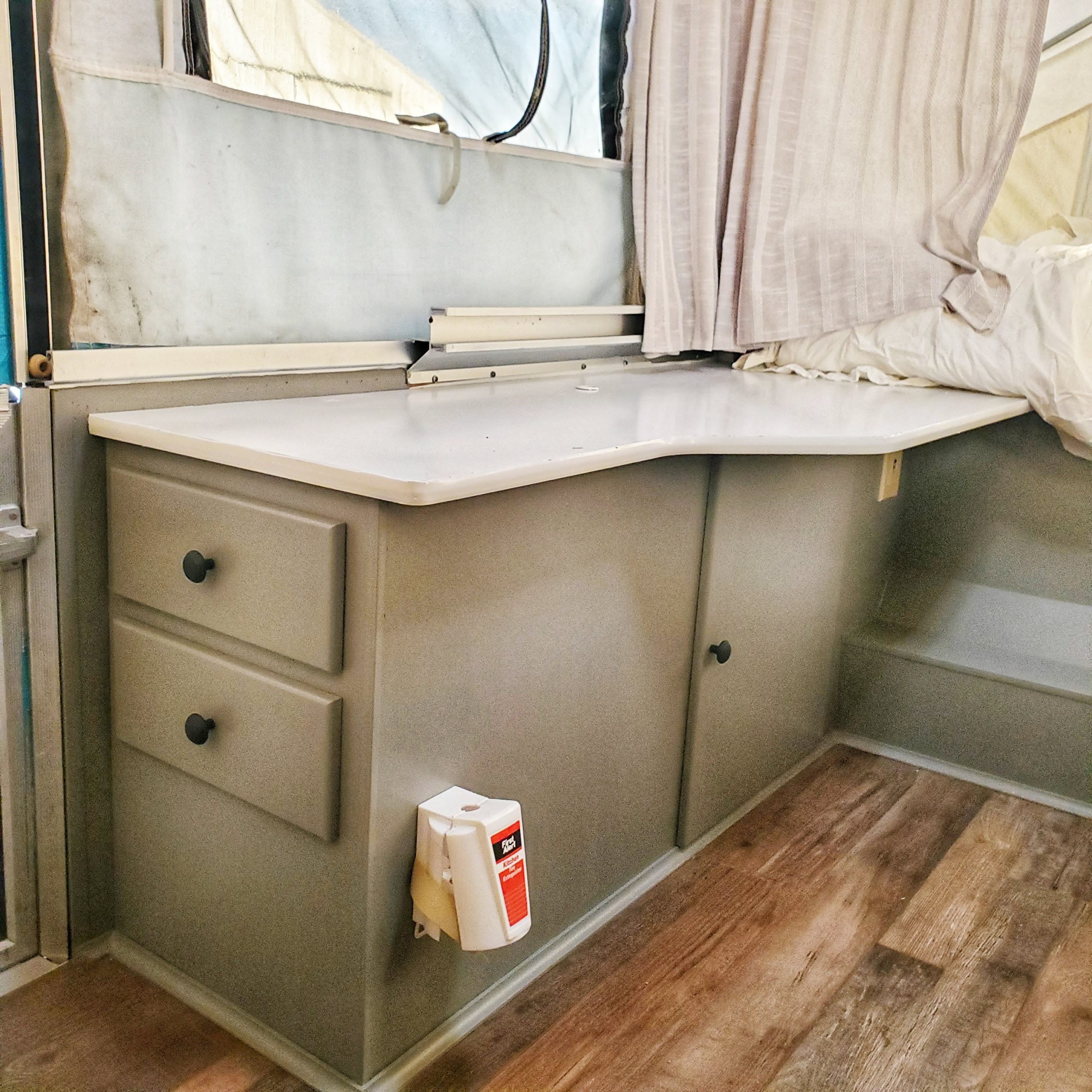 Update your RV with a modern farmhouse look with gray painted cabinets, curtains, a new wood stained table, and updated countertops for less than $500!